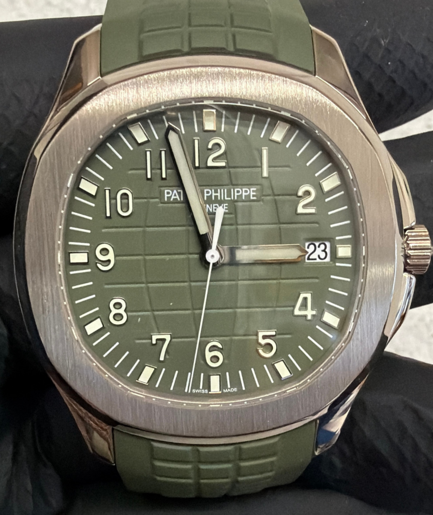 Patek Philippe wristwatch with olive green dial and green strap, brushed metal case, large Arabic numerals and a date window showing 23 at 3 o'clock