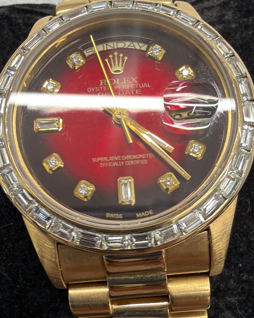 Gold Rolex Oyster Perpetual Date watch with a red dial, diamond hour markers, and a diamond-studded bezel on a gold bracelet.